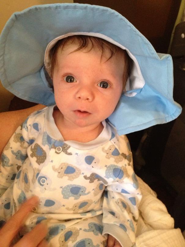 Adorable baby with deep blue eyes, wearing light blue and white elephant pajamas and a floppy blue hat.