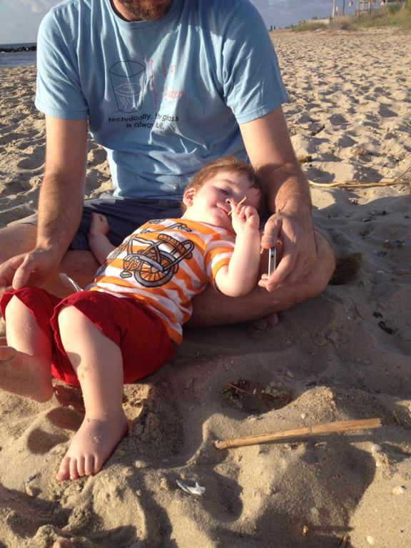 Father and son on a sandy beach. Super cute kid lounges on a sandy beach with his father.