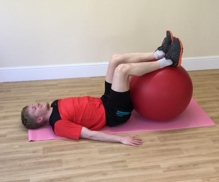 Lying Bridge With your arms resting either side of your body as shown, simultaneously tilt the tail bone towards the ceiling, roll the ball away and lengthen your legs until the knees