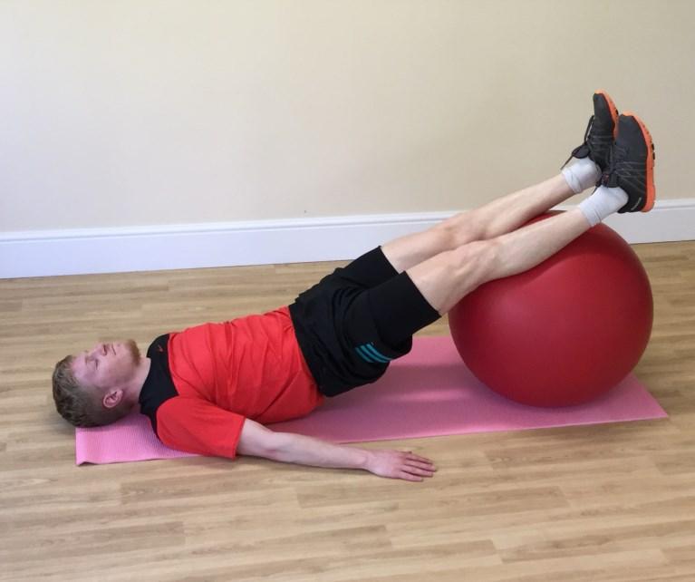To return, bend the knees and roll the ball backwards (feeling the hamstrings/back of thighs engage) whilst simultaneously rolling the spine down onto the floor.