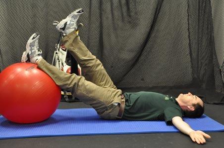 Start by lying on your back with your feet up on a Swiss ball and your arms crossed over your chest.