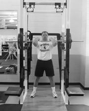 With the bar positioned overhead and the shoulders and elbows locked, bend at the knees and