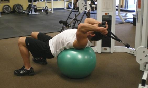 26 Ball Rope Crunches - Lie across a fitness ball while holding your hands on a rope attached to a cable pulley.