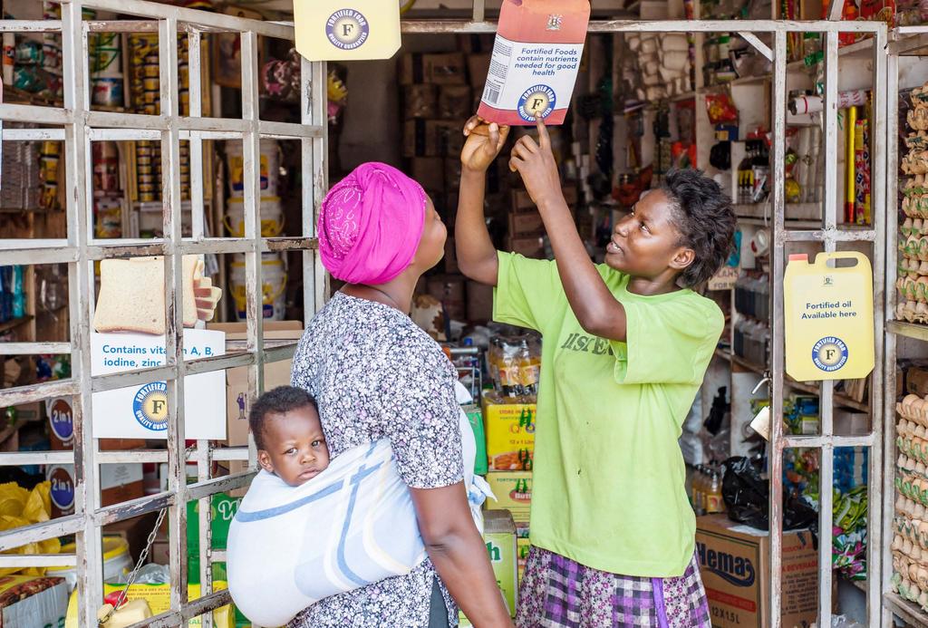 Shopkeeper Winnie Nanyonga explains food fortification to her client, Jessica Namusoke.