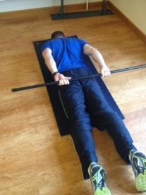 Prone Shoulder Extension Lying on your front forehead on a block arms straight by your sides holding a weighted bar.