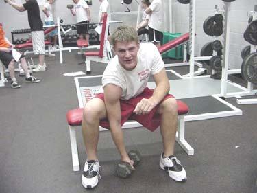Grant is preparing to do the SEATED CONCENTRATED BICEP CURL. He is holdin g the dumbbell, palm up.
