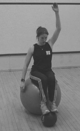 Seated balance with feet on medicine ball Seated on swiss ball with feet on medicine ball. Level 1: Start with arms above head, and sitting directly onto sit bones.